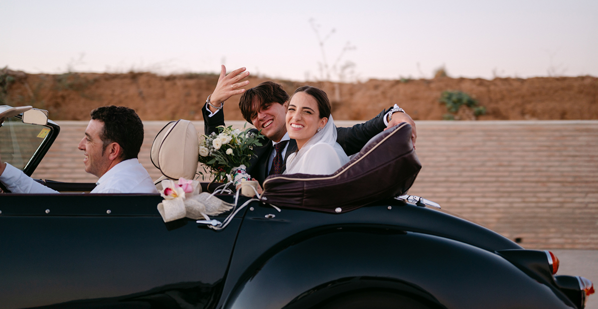 Fotografía divertida de boda novios saludando desde el coche al fotografo de boda